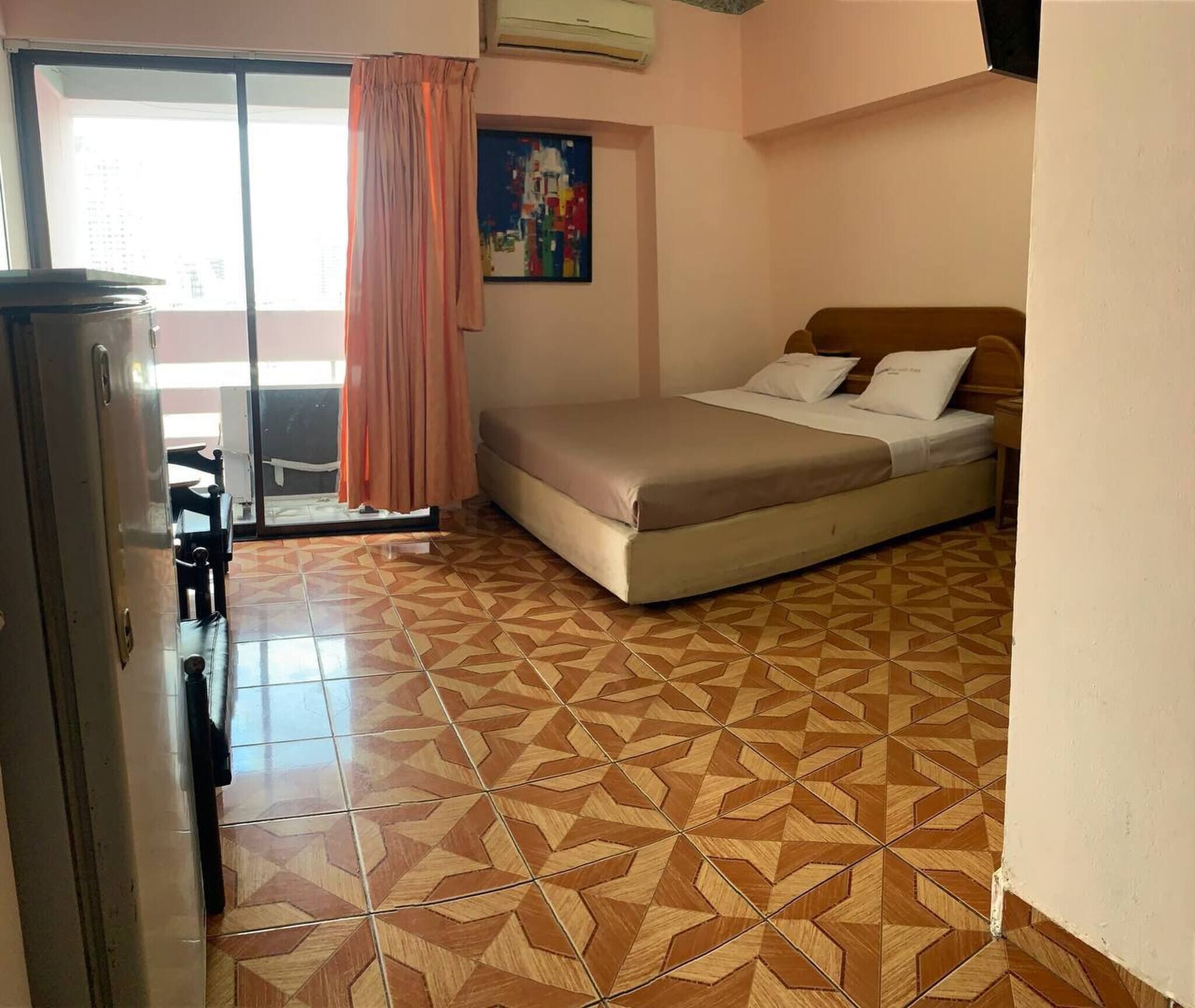 A bedroom with a bed, a window with curtains, a tiled floor, and a painting on the wall.