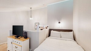 A bedroom with a bed, a TV, a dresser, and a wall-mounted light fixture. - Okanagan - Hilltop Hideaway Condo - Legacy 401A (Beaverdell)