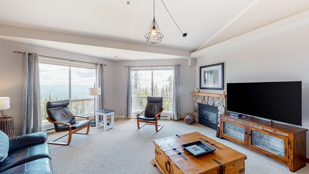 A spacious living room with a large TV, comfortable seating, a fireplace, and a scenic view. - Okanagan - Hilltop Hideaway Condo - Legacy 401A (Beaverdell)