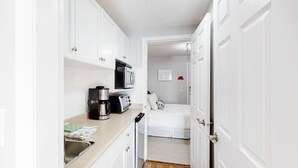 Uma cozinha compacta com armários brancos, cafeteira, torradeira e micro-ondas.