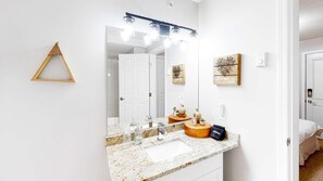 A modern bathroom with a large mirror, vanity, and a wooden vanity with a makeup bag. - Okanagan - Hilltop Hideaway Suite - Legacy 401B (Beaverdell)