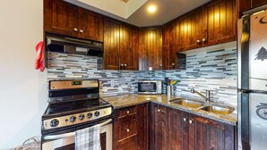 A kitchen with wooden cabinets, a black stove, a microwave, and a stainless steel sink. - Okanagan - Lac Le Jeune at Cabin 4 (Kamloops)
