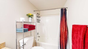 A bathroom with a toilet, a shower, and a metal shelf holding towels. - Okanagan - Lac Le Jeune at Cabin 4 (Kamloops)
