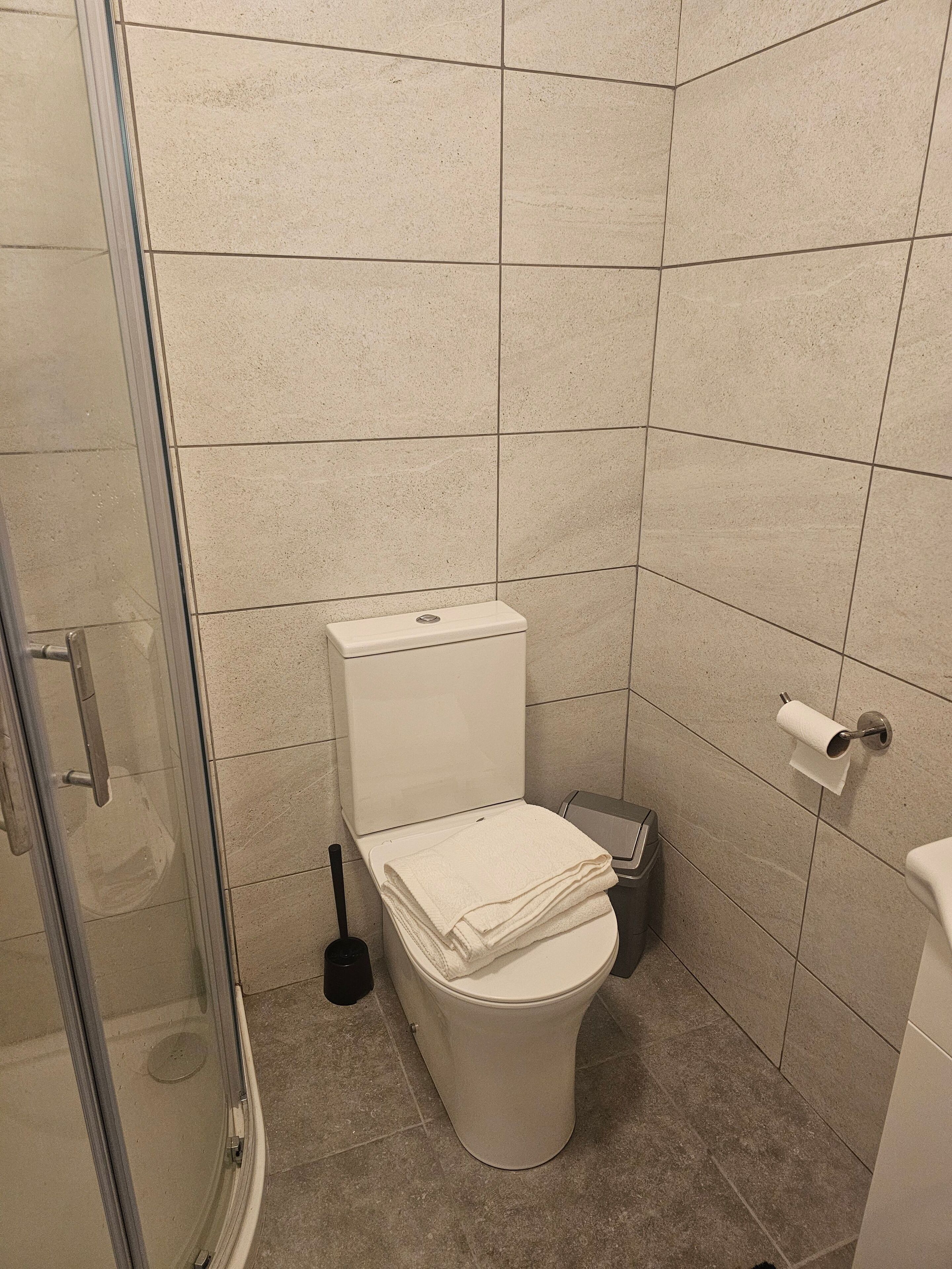 Une petite salle de bain comprenant des toilettes, une douche à parois de verre et un porte-rouleau de papier toilette.