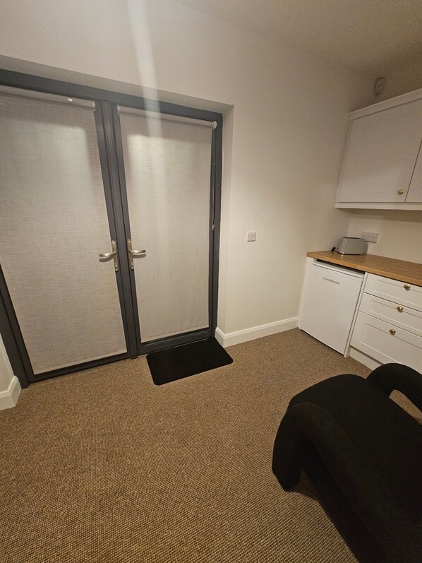 Une pièce avec une porte-fenêtre coulissante, un meuble blanc avec des tiroirs, un grille-pain posé sur le plan de travail et une chaise noire.