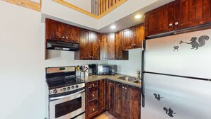 Una cocina compacta con armarios de madera, un refrigerador de acero inoxidable, un microondas, una estufa y un lavamanos.