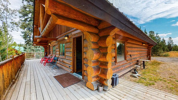Una cabaña de madera con terraza, asientos exteriores y vistas al bosque circundante.