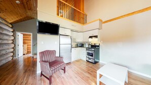 Cocina compacta con horno, microondas y refrigerador integrados. Una silla a rayas se encuentra en la zona de estar, y se ve una mesa blanca.