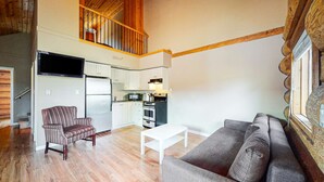 Amplia sala de estar con una escalera de madera, una cocina con armarios blancos, una mesa de comedor y un sofá.