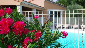 A pool area with a white fence, pink flowers, and a building with a tiled roof. - Blue Hills Residence with Scenic Views (Sampzon)