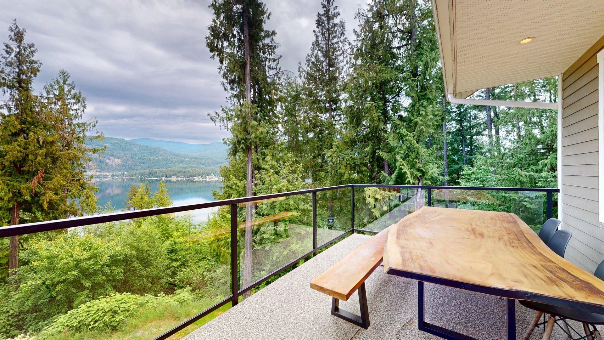 Un balcón con mesa y banco de madera, con vistas a un lago y montañas boscosas.