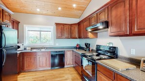 A kitchen with wooden cabinets, a stainless steel stove, a dishwasher, and a window with a view of greenery. - Okanagan - IKES Retreat (Kootenay Boundary)