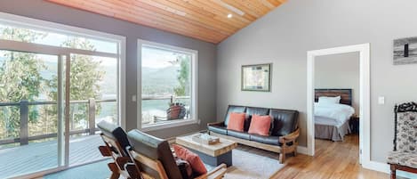 Un salón amplio con un ventanal grande, un sofá de cuero negro, sillas de madera y una mesa de centro de madera.