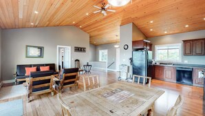 A spacious living area with a wooden ceiling, a dining table, and a kitchen with wooden cabinets. - Okanagan - IKES Retreat (Kootenay Boundary)