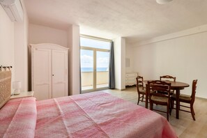 A bedroom with a bed, a wardrobe, a dining table with chairs, and a large window with a view. - Con vista mare, terrazza, aria condizionata (Castelsardo)