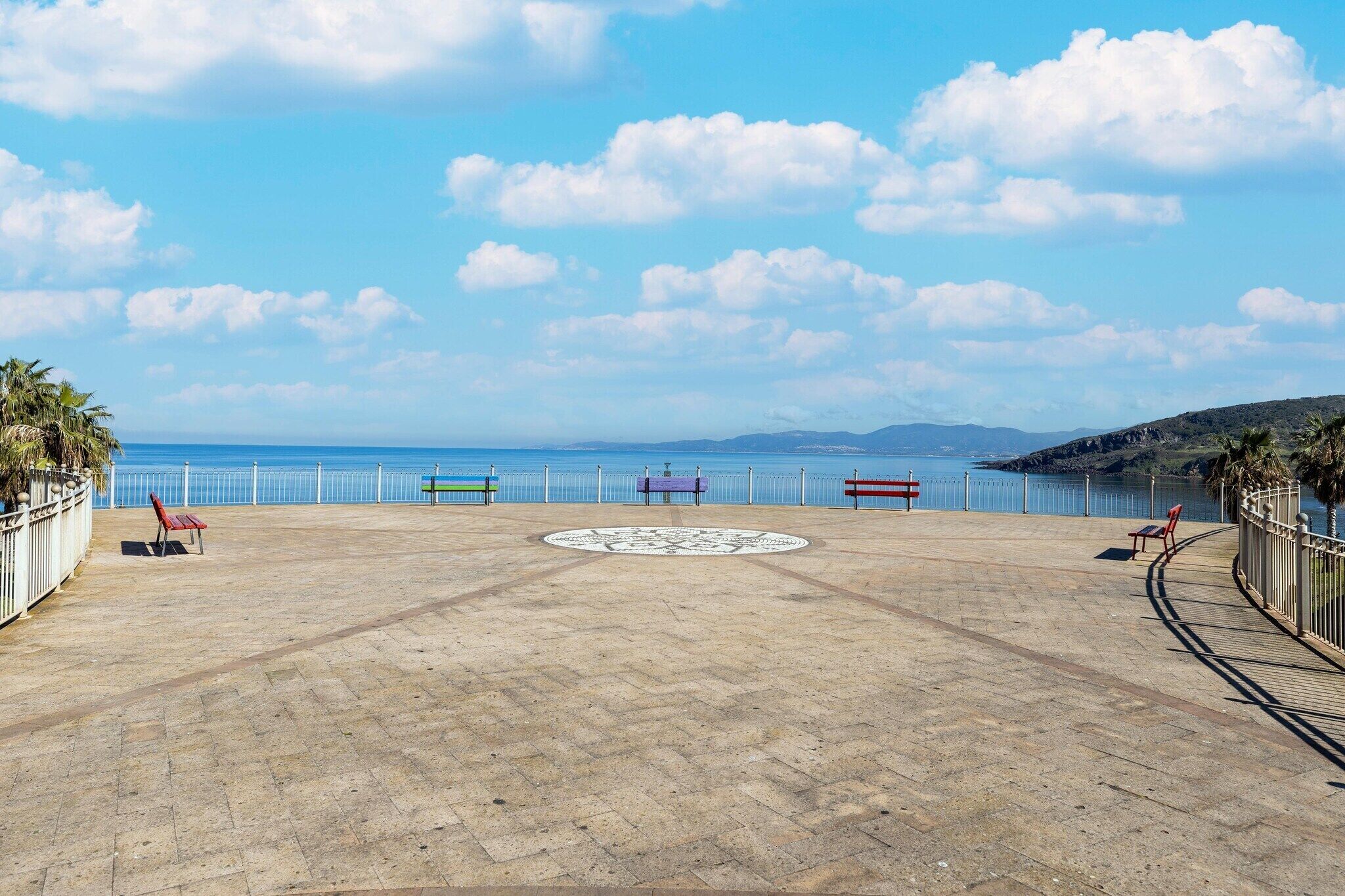 A paved promenade with benches, a circular decorative pattern, and a view of the sea.