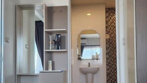 Hotelkamer met een bed, nachtkastje met lamp en plant, badkamer met wastafel en spiegel, en douche.