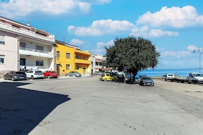 A coastal street with parked cars, a yellow building, and a tree. - Con vista mare, terrazza, aria condizionata (Castelsardo)