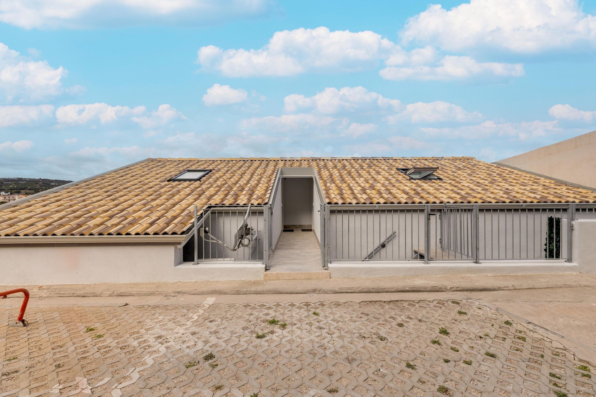A building with a tiled roof, a central entrance, and a paved ground.