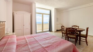 A bedroom with a bed, a wardrobe, a dining table with chairs, and a large window with a view. - Con vista mare, terrazza, aria condizionata (Castelsardo)