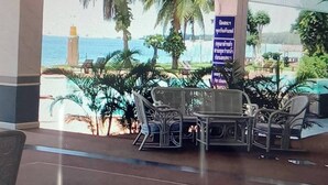 A waiting area with a view of palm trees and a pool, featuring several chairs and a table.
