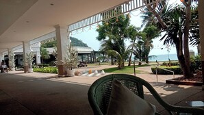 A covered outdoor area with a seating area, palm trees, and a view of the sea.
