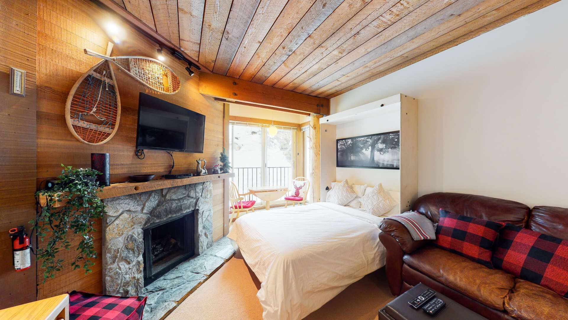 A cozy room with a stone fireplace, a bed, a leather sofa, and a television mounted on the wall.