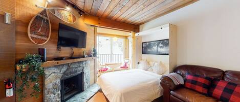 A cozy room with a stone fireplace, a bed, a leather sofa, and a television mounted on the wall.