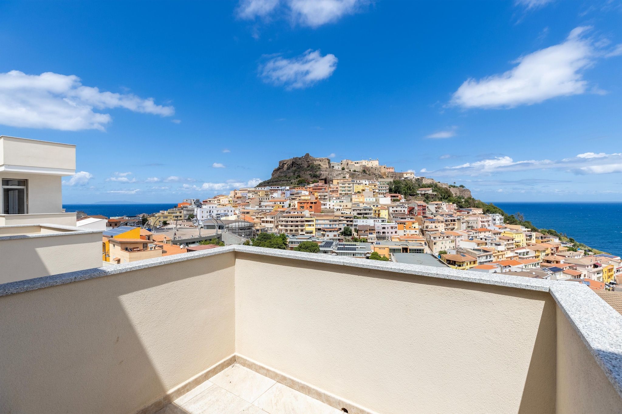 Une ville côtière dotée d’une imposante forteresse perchée sur une colline, offrant une vue sur la mer et un balcon donnant sur la ville.