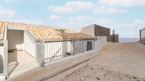A building with a tiled roof, a metal fence, and a paved area leading to a gate. - Apartment with sea view and terrace (Castelsardo)