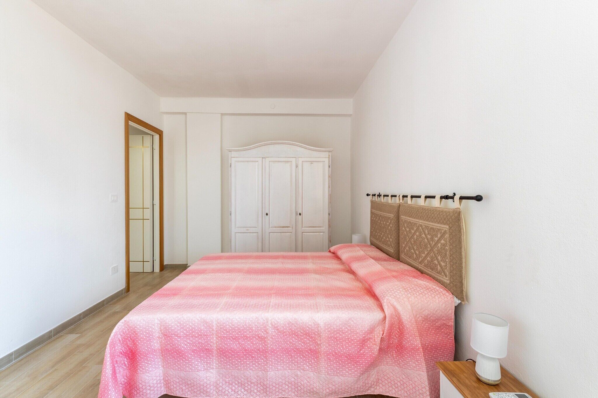 A bedroom with a bed, a wardrobe, a bedside table with a lamp, and a door.
