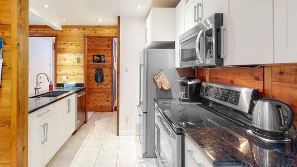 A modern kitchen with wooden paneling, stainless steel appliances, and a marble countertop. - Okanagan - Ponderosa Inn 408 - Hilltop Hideaway (Big White Mountain)