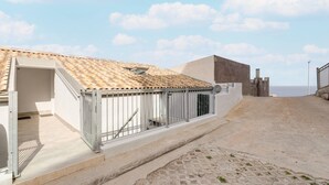 A building with a tiled roof, a metal fence, and a paved area leading to a gate. - Apartment with sea view and terrace (Castelsardo)