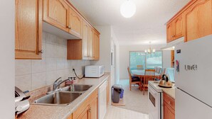 Una cocina con armarios de madera, microondas, fregadero y comedor con mesa y sillas.