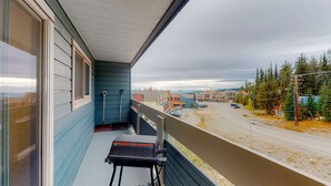 Un balcón con vista a una carretera y edificios, una parrilla y una ventana con persianas.