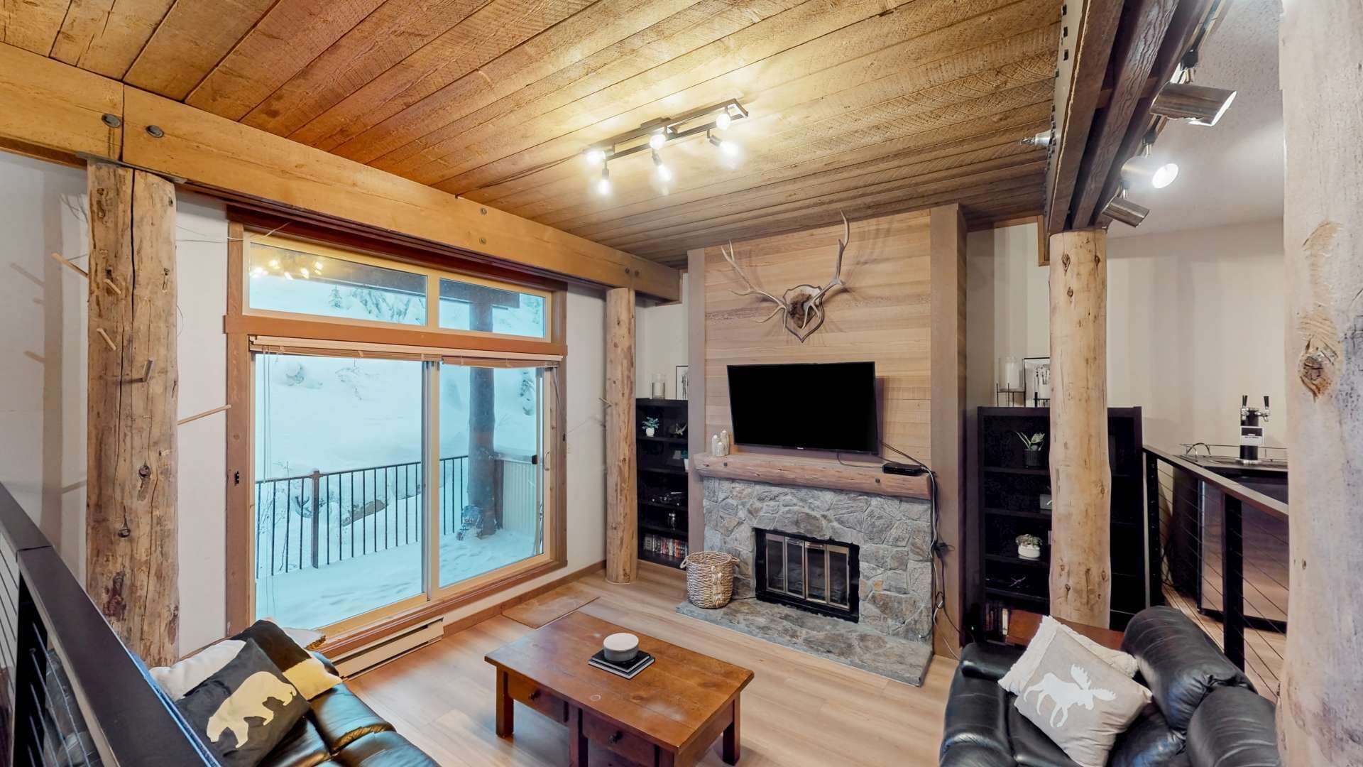 Una sala de estar acogedora con una chimenea de piedra, un televisor grande montado encima y un techo de madera.