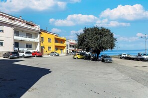Una calle costera con coches estacionados, un edificio amarillo y un árbol.