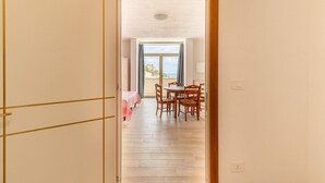 Una porta aperta che dà su un'area pranzo con tavolo e sedie, vista all'esterno e un balcone con tavolo e sedie.