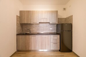 Een kleine keuken met houten kastjes, een roestvrijstalen spoelbak en een zwarte koelkast.