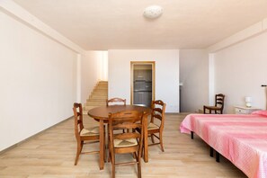 Una habitación con una mesa de comedor y sillas, una cama con cubrecama rosa, una mesita de noche pequeña y un espejo en la pared.