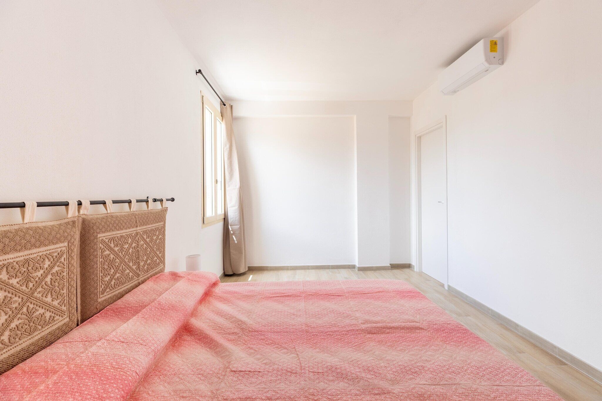 A bedroom with a bed, a window with curtains, a white door, and a wall-mounted air conditioner.
