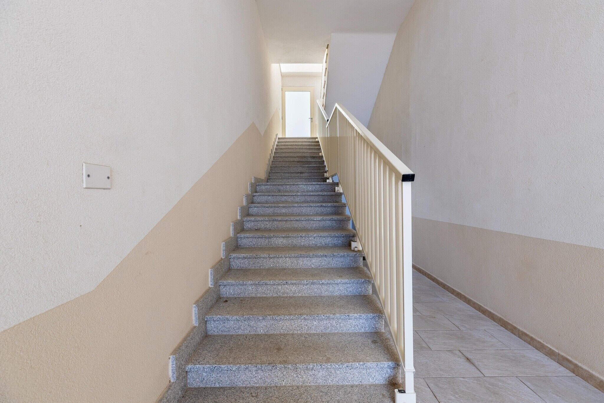 A staircase with a handrail, carpeted steps, and a light switch on the wall.