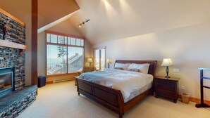 A bedroom with a large bed, a stone fireplace, and a view of the outside. - Okanagan - Northern Star (Kootenay Boundary E)