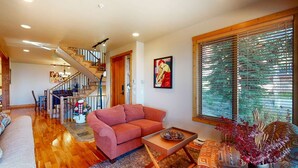 A spacious living room with a wooden staircase, a large window with blinds, and a red sofa. - Okanagan - Northern Star (Kootenay Boundary E)