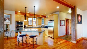 A spacious kitchen with wooden cabinets, a central island with stools, stainless steel appliances, and pendant lighting. - Okanagan - Northern Star (Kootenay Boundary E)