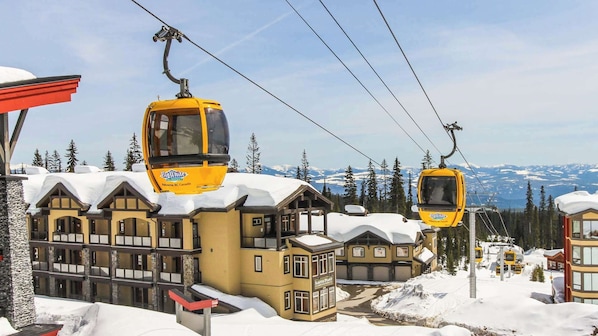 A ski resort with yellow cable cars and a lodge with multiple windows and a snow-covered roof. - Okanagan - Raven 104 (Big White Mountain)