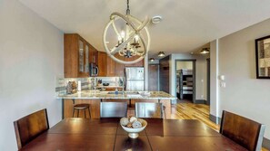 A modern kitchen with wooden cabinets, a marble countertop, and a unique rope chandelier. - Okanagan - Raven 104 (Big White Mountain)