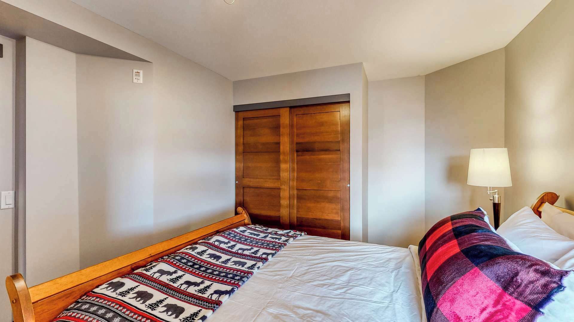 A bedroom with a bed, a wooden headboard, a bedside lamp, and a wardrobe.