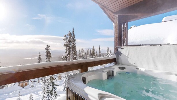 A hot tub with a wooden deck and a view of snow-covered trees and mountains. - Okanagan - Powder View 5 (Beaverdell)