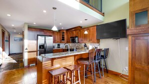 A modern kitchen with wooden cabinets, a stainless steel refrigerator, a microwave, and a large island with bar stools. - Okanagan - Powder View 5 (Beaverdell)